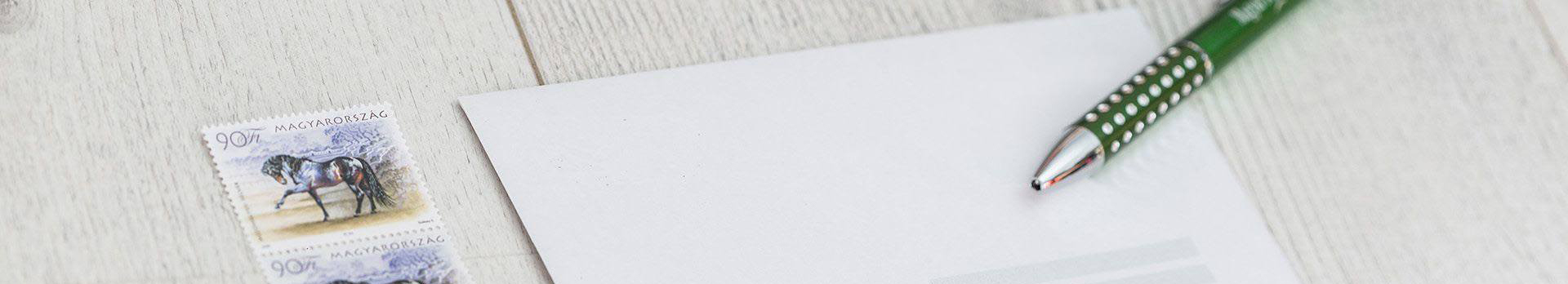 A képen egy boríték, egy toll és néhány bélyeg látható.